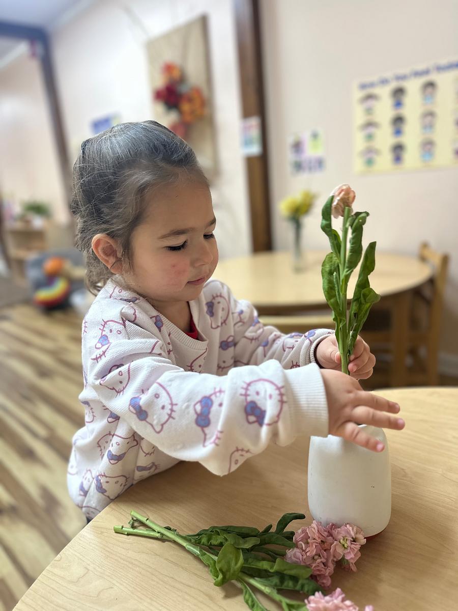 A young girl playing with a small green plant indoors.