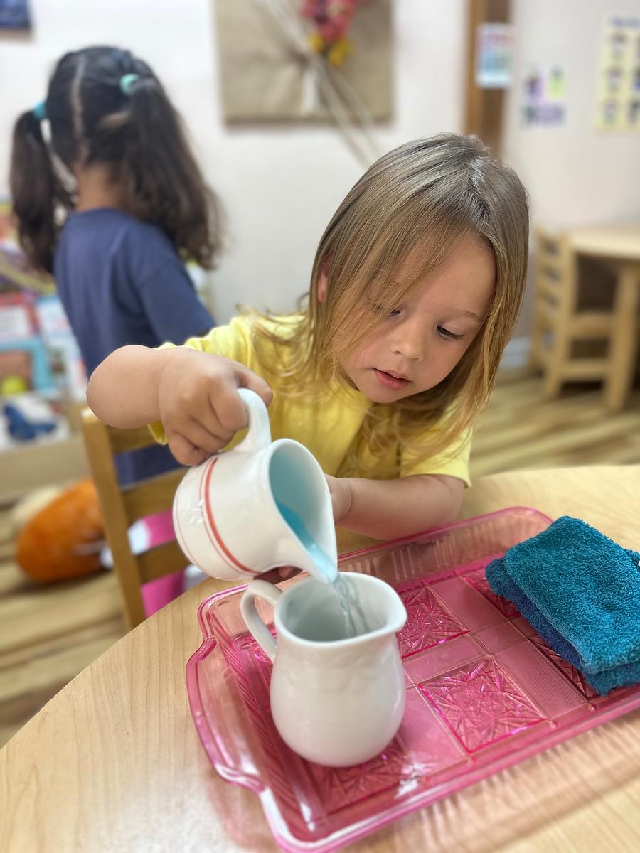 A young girl pouring liquid from a blue cup into a white cup.