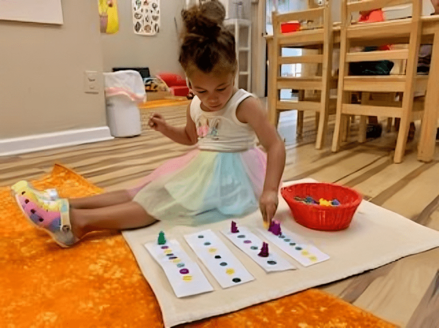 A young child painting colorful dots on paper while sitting on the floor.