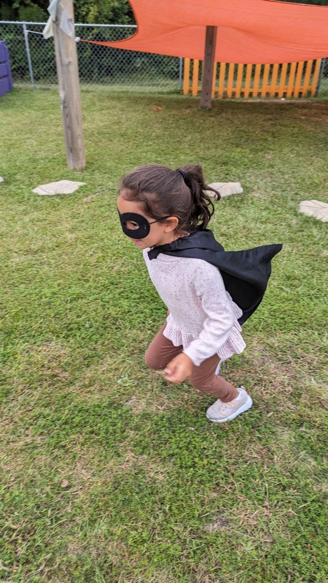 A young girl wearing a mask, playing outdoors on grass.