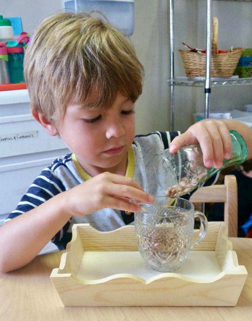 Young boy pouring water into a container at a table.