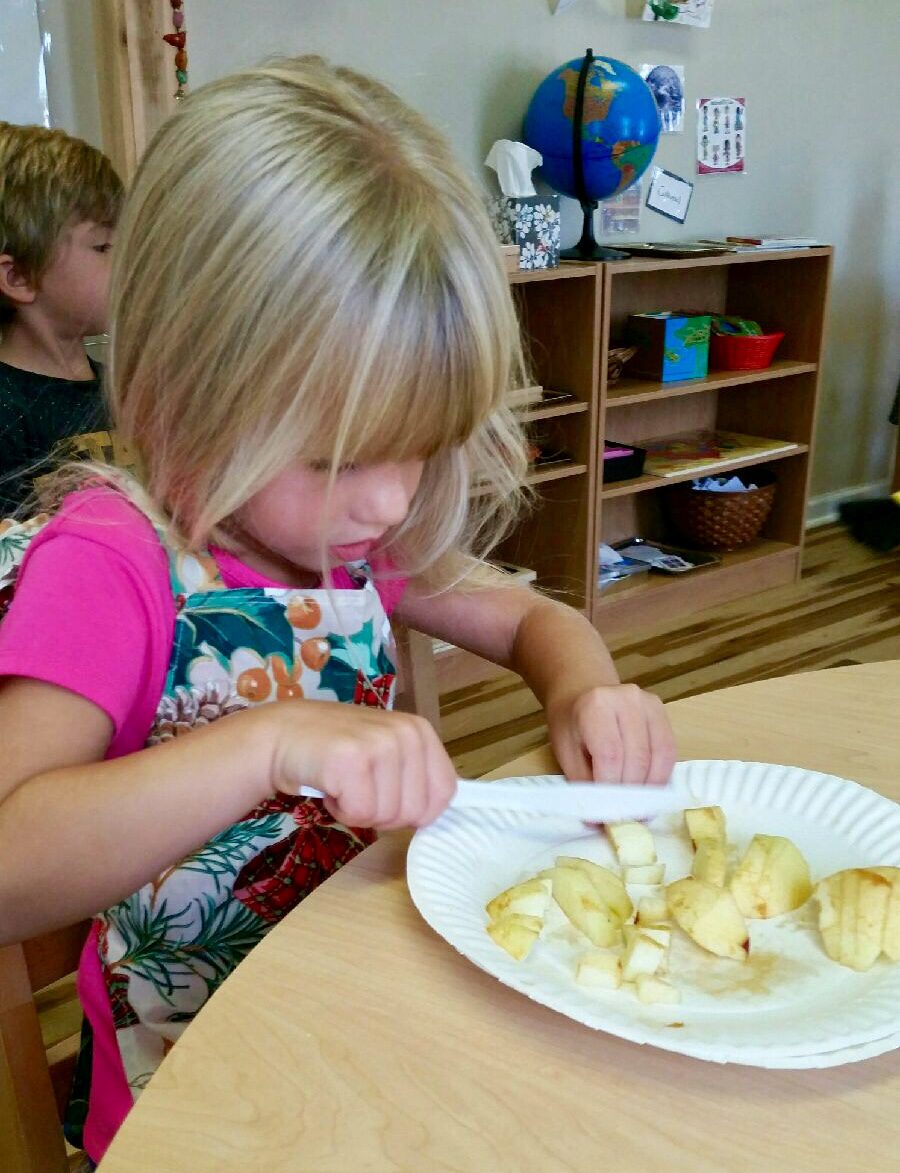 A young girl peeling or cutting bananas at a table.