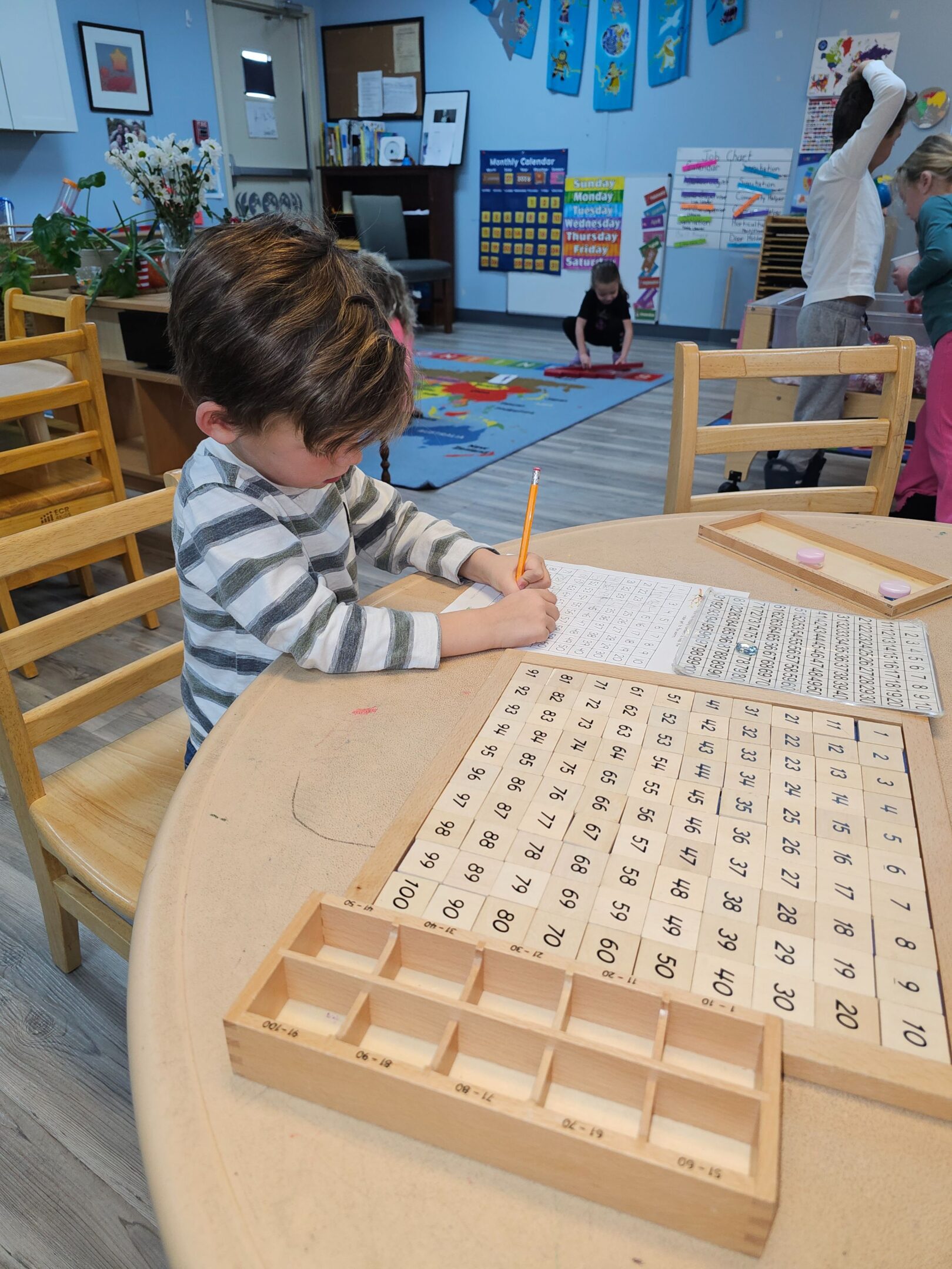 A child practicing writing numbers at a classroom table.